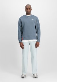 Pilka prakaitinė maikutė su braižytomis rankovėmis ir apačia, uždėta ant baltos marškinėlių. Šviesiai mėlynos džinsinės kelnės ir pilki sportbačiai užbaigia aprangą.