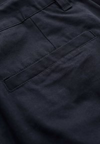 Zwarte stof met een gladde textuur, voorzien van een enkele paspelzak. De stiksels zijn net en de stof lijkt duurzaam en flexibel te zijn.