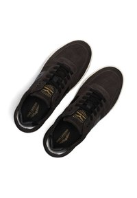 Bruine suède sneakers met zwarte leren accenten, ronde neus, vetersluiting en witte rubberen zool. Gouden branding op de tong.