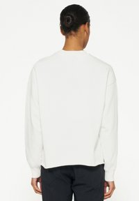 Witte, lange mouw sweatshirt met ronde hals, rechte zoom en een ontspannen pasvorm. De achterkant heeft een gladde textuur en minimale details.