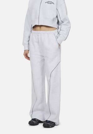 Felpa grigia corta con zip e logo nero, abbinata a pantaloni della tuta grigi con tasche laterali e cuciture nere a contrasto.