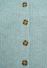 Ανοιχτό μπλε πλεκτό ζακέτα με έξι στρογγυλά μάρμαρα κουμπιά σε σχέδιο χελώνας και ριμπ υφή σε όλο το ύφασμα.
