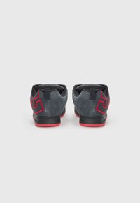 Grå suede sneakers med sorte detaljer og en rød sål. Har et iøjnefaldende rødt logo på hælen og en polstret krave for komfort.