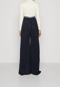 Námořnické široké kalhoty s vertikálními zlatými pruhy, vybavené vysokým ribovaným pasem a hladkou texturou.