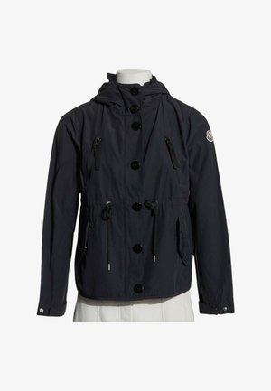 Sort hættejakke med knapper foran, lynlåslommer på brystet, snøre i taljen og logo på venstre ærme, vist på en mannequin.