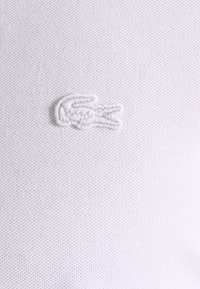 Polo shirt blanc texturé avec un petit logo brodé d'un crocodile dans le coin supérieur gauche.