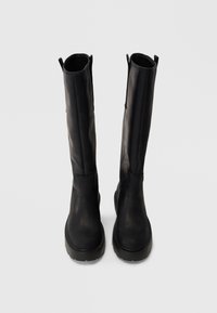 Black knee-high boots made of smooth leather with a rounded toe and textured sole. Features minimal stitching and side zippers for wearability.