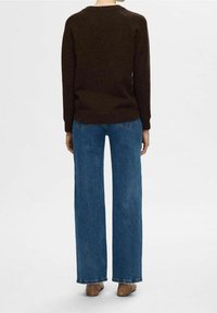 Dunkelbrauner Strickpullover mit langen Ärmeln, kombiniert mit blauen weiten Jeans. Sichtbare Nähte und lockere Passform, die Stofftextur ist nicht detailliert.