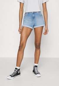 Jeansshorts i ljusblått, uppvikta fållar, hög midja. Kombinerat med svarta hög-top sneakers och vita strumpor. En enkel grå t-shirt.