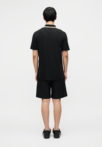 Μαύρο πόλο πουκάμισο και σορτς, με απλό σχέδιο, άνετη εφαρμογή και ελάχιστη υφή. Συνδυασμένα με μαύρα παπούτσια, από πίσω όψη.