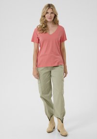 Korálové tričko s výstřihem do V spárované se světle olivovými cargo kalhotami s bočními kapsami, doplněné béžovými kotníkovými botami. Hladká tkanina a uvolněný střih.