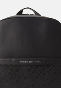 Sac à dos noir en matériau synthétique texturé, doté d'un panneau supérieur lisse et d'un logo avec des accents de motif en relief.