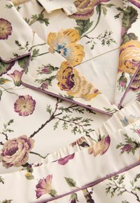 Tessuto con motivo floreale caratterizzato da uno sfondo chiaro con fiori viola, gialli e verdi. Texture satinata con dettagli arricciati e piping in satin.