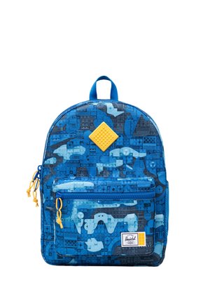 Sac à dos bleu avec motif de briques de type LEGO, tirettes de fermeture éclair jaunes, poche avant et un patch carré jaune au centre supérieur.