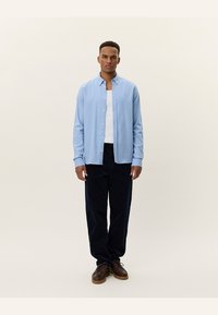 Light blue button-up shirt with long sleeves, worn over a white undershirt, paired with dark corduroy pants and brown shoes.