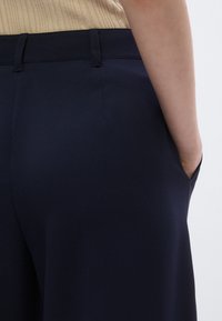 Navy blue trousers made from a smooth fabric, featuring a tailored fit, side pocket, and a waistband with belt loops.