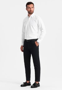 Camicia bianca con bottoni, pantaloni neri, cintura nera e scarpe nere. Design semplice, vestibilità su misura, tessuto morbido e stile classico.