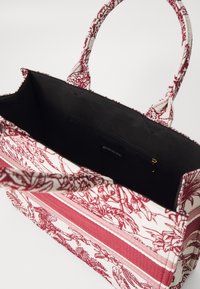 Rød og hvid mønstret stof tote bag med to hanke, som har en sort indvendig og en lynlåslomme. Stribet design fremhæver. 