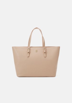 Beige læder-tote taske med to skulderremme og lille guld logoemblem midt foran på ensfarvet baggrund.