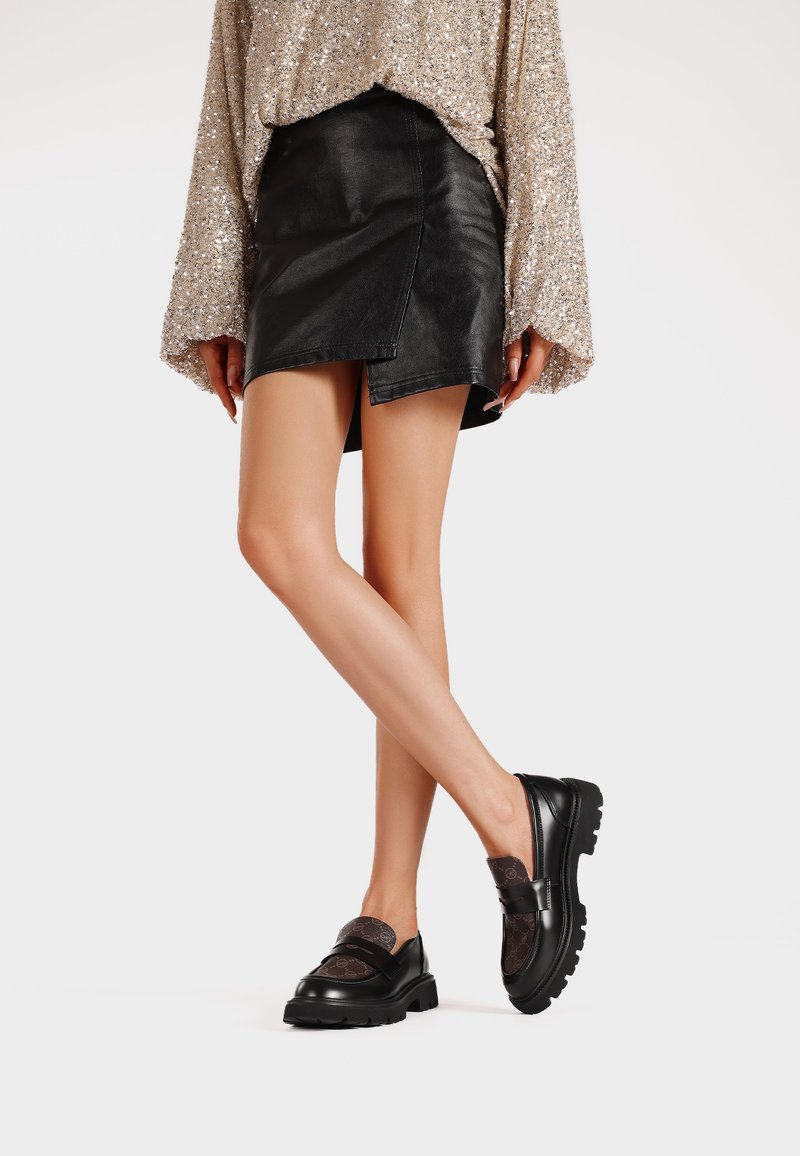 Mocassini neri con un accento marrone testurizzato e suola in gomma, abbinati a una gonna di pelle nera e a un top luminoso chiaro.