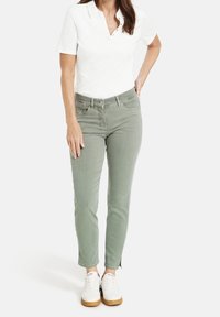 Svetle zelené džínsy s úzkým střihem, detaily kapes a mírným třepením na lemu, spárované s bílým polo tričkem a bílými teniskami.