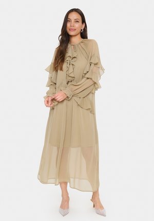 Abito lungo color khaki con dettagli arruffati lungo le maniche e il colletto, realizzato in tessuto leggero, caratterizzato da una silhouette fluttuante e strati trasparenti.