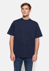 Tricou din bumbac bleumarin, cu mâneci scurte, guler rotund, croială lejeră, cu un textură netedă și fără modele sau accente vizibile. Asortat cu blugi din denim.