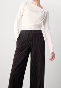 Lange mouwen, off-white top met gedrapeerde halslijn, gecombineerd met zwarte wijde broek met witte streepjes en zijzakken.