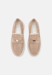 Beige suède slip-on sko med en teksturert overflate, rund tå, og dekorativ stropp med gullaccent. Polstret hvit såle.
