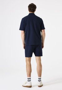 Camisa polo azul marino y pantalones cortos a juego, hechos de tejido tejido, con un corte relajado, mangas cortas y un cuello plano. Llevado con zapatillas blancas.