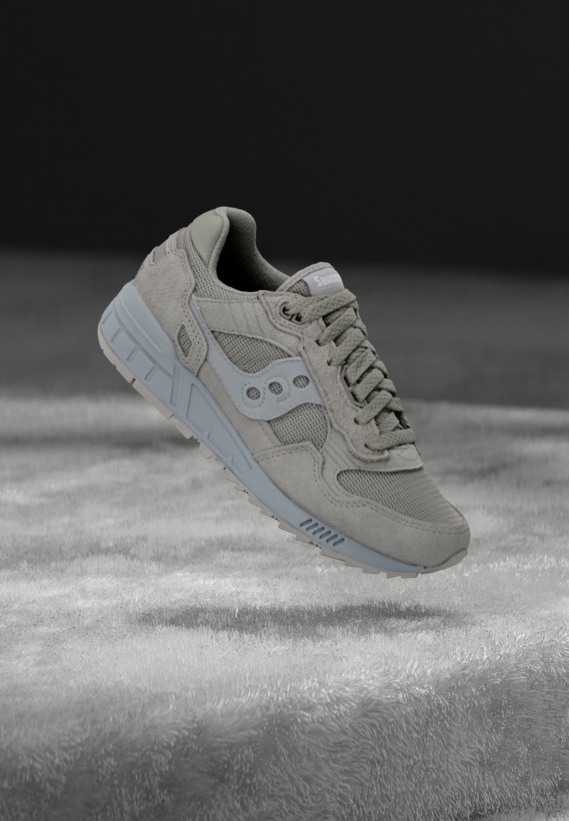 Grauer Sneaker aus Wildleder und Mesh, mit hellgrauer Sohle, strukturierten Akzenten und drei runden Belüftungslöchern an der Seite.