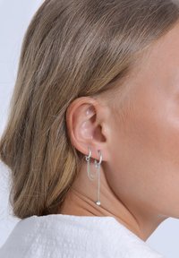 Cercei rotunzi din argint, cu accente de lanț și un pandantiv din cristal, evidențiind un design minimalist și o textură metalică netedă.