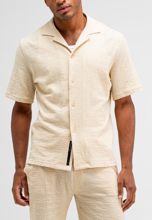 Short-sleeve, light beige shirt made of textured fabric with a slightly structured design. Features a camp collar and button front closure.