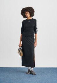 Black textured sweater with white stripes on sleeves, paired with a black skirt featuring side slits, gray sneakers, and a brown handbag.