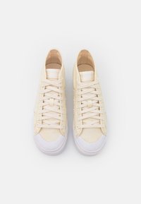 Ljusbeige kanvas sneakers med texturerad ovandel, vit gummitåhätta och platta snören. Minimalistisk design utan synliga logotyper.