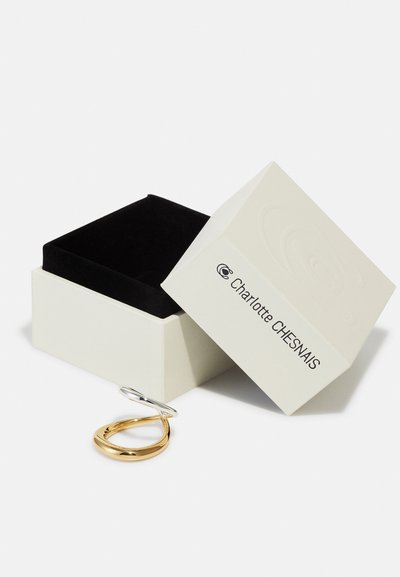 Offene weiße Schmuckbox mit schwarzem Innenfutter und einem zweifarbigen Gold- und Silberring daneben, Marke Charlotte Chesnais.