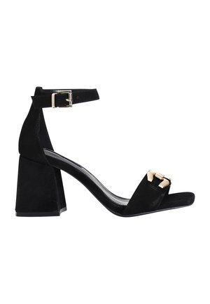 Sandali con tacco alto in suede nero, con punta quadrata e tacco spesso. Presentano una cinghia alla caviglia con una fibbia metallica e un accento decorativo in oro.