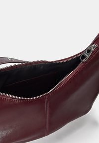 Borsa in pelle marrone con chiusura a zip, texture liscia e dettagli in zip color argento. L'interno presenta una fodera in tessuto nero e una tasca.