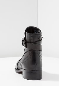 Svart läderankelstövel med rundad tå, dekorativa perforeringar och en sidodragkedja med spännedetalj. Låg klack med staplad design.