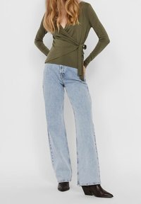 Oliivinvihreä, pitkähihainen kietaisupaita, jossa solmimisyksityiskohta, yhdistetty vaaleansinisistä levenevistä farkuista ja mustista, kärjistetyistä korkokengistä.