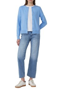 Lichtblauwe gebreide cardigan met lange mouwen, ronde halslijn en knoopsluiting, gecombineerd met lichtblauwe rechte spijkerbroek en witte sneakers.
