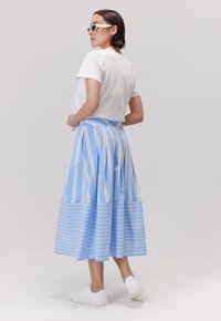 Niebieska spódnica w paski z białymi poziomymi i pionowymi liniami, zestawiona z krótkim białym t-shirtem i białymi sneakersami. Gładka tekstura materiału.