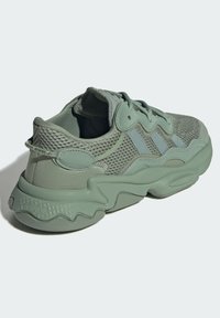 Jasnozielony sneaker z siateczki z teksturowaną podeszwą, gładkimi akcentami i trzema tonowanymi paskami po boku. Okrągły nosek i wiązanie na sznurówki.