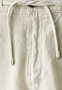 Shorts en lin beige avec une taille à cordon de serrage, une poche latérale et des détails de couture visibles, mettant en valeur une finition en tissu texturé.