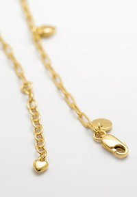 Catena in metallo dorato con un ciondolo a forma di cuore e un moschettone. Presenta anelli allungati e una superficie testurizzata. Design minimalista.