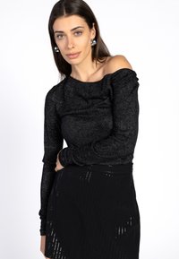 Zwarte off-the-shoulder top met lange mouwen, gemaakt van glanzende stretchstof. Heeft ruches langs de schouders en een zachte textuur.