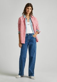 Camicia a fiori rossi sopra una camicia di jeans leggera blu, canotta bianca e jeans blu a vita alta. Sneakers bianche completano l'outfit.