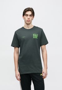T-shirt cinzento escuro de algodão com marca e texto Nike em verde néon. Mangas curtas, gola redonda e corte confortável. Sem padrões visíveis.