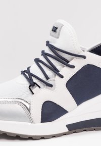 Chaussure de sport blanche et marine avec dessus en mesh, lacets marines et semelle coussinée, montrant les détails latéraux et avant.