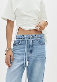 Helle blaue Jeans aus Denim mit entspannter Passform, featuring einen Kordelzugverschluss, fünf Taschen und dezenten Verwaschungen. Kombiniert mit einem weißen Hemd.